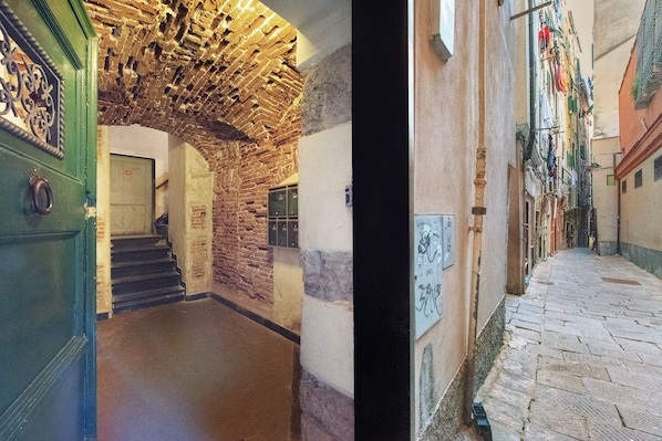 A narrow stone corridor with a brick archway and a door with a green frame.