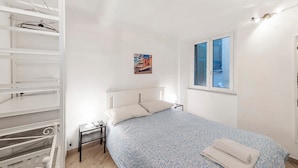 A bedroom with a bed, a nightstand, a window with shutters, a wall-mounted picture, and a white wardrobe with a mirror. - Apartment 'Modern Flat in The Centre Of Genoa' with Wi-Fi and Air Conditioning (Genova)