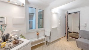 A modern, well-lit room with a white bench, a small table with a coffee maker, and a door leading to another room. - Apartment 'Modern Flat in The Centre Of Genoa' with Wi-Fi and Air Conditioning (Genova)