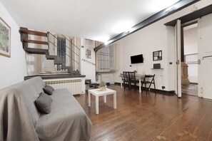 A living room with a sofa, a dining table, a staircase, and a kitchen area.