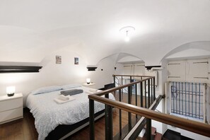 A bedroom with a bed, bedside tables, a window with bars, a staircase, and a ceiling light.