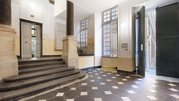 Un pasillo con piso a cuadros, una escalera y una puerta que da al exterior.