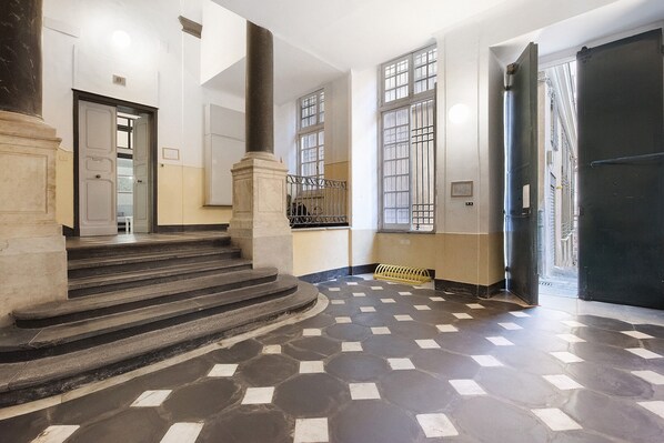 A hallway with a checkered floor, a staircase, and a door leading outside.
