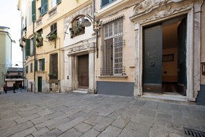 A narrow cobblestone street with historic buildings, a visible entrance with a metal gate, and a door with a textured surface.