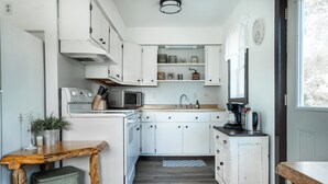 A compact kitchen with white cabinets, a wooden table, and a coffee machine.