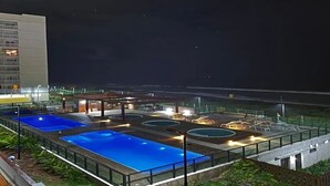 A rooftop pool area with multiple pools and lounge seating, surrounded by a glass railing and illuminated by artificial lighting. - Feet in the sand - near Beto Carrero (Barra Velha)