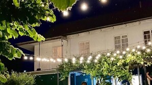 An outdoor seating area with string lights, a stone wall, and a building in the background. - Debatoun (Debet)