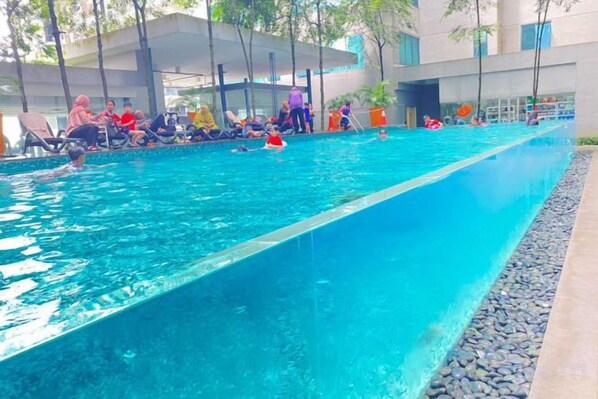 A swimming pool with people around it, a covered seating area, and a building in the background. - Summer Suites KLCC by Luna (Kuala Lumpur)