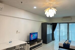 A modern hotel room with a flat-screen TV, a dining table, a sofa, and a large window with curtains. - Summer Suites KLCC by Luna (Kuala Lumpur)