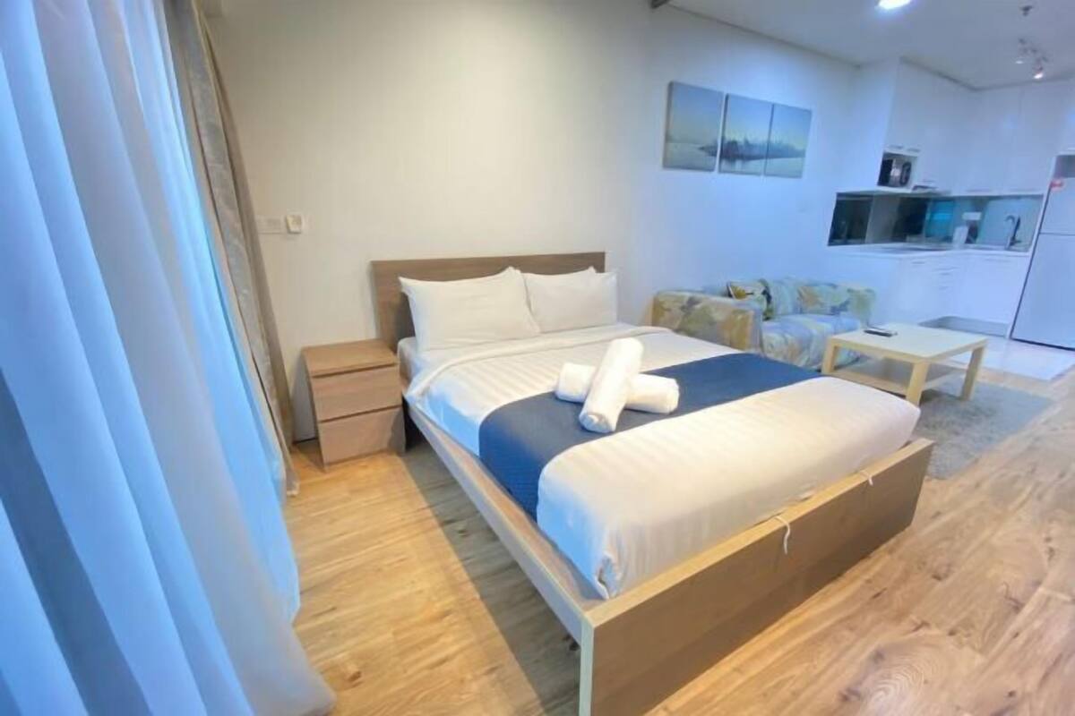 Une chambre d’hôtel moderne avec un lit en bois, un petit bureau, un canapé et une kitchenette.