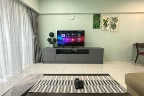 Un salon avec un téléviseur à écran plat posé sur un meuble de télévision gris, un tapis à motifs et une télécommande sur une table basse.