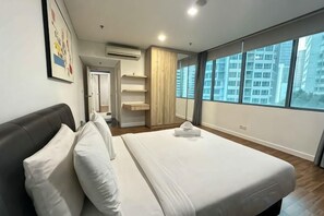 A modern hotel room with a large bed, a wardrobe, a bathroom, and a view of the city. - Summer Suites KLCC by Luna (Kuala Lumpur)