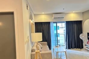 A modern hotel room with a sofa, a small table, a lamp, and a fan. - Summer Suites KLCC by Luna (Kuala Lumpur)