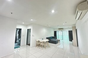 A modern living room with a dining area, a sofa, and a large window. - Summer Suites KLCC by Luna (Kuala Lumpur)