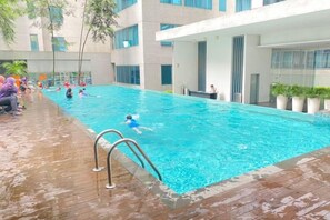 An indoor swimming pool with a wooden deck and a modern building in the background. - Summer Suites KLCC by Luna (Kuala Lumpur)