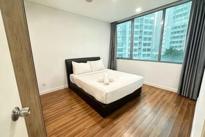 A bedroom with a bed, wooden flooring, a window with curtains, and a view of buildings. - Summer Suites KLCC by Luna (Kuala Lumpur)