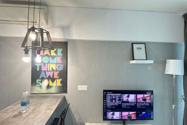 A modern room with a flat-screen TV, a wooden desk, a wall-mounted shelf, and a pendant light. - Summer Suites KLCC by Luna (Kuala Lumpur)