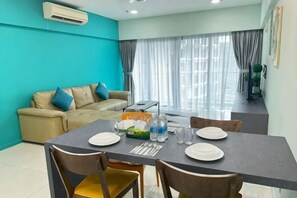 A dining area with a table set for four, a sofa, and a window with curtains. - Summer Suites KLCC by Luna (Kuala Lumpur)