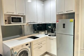 A compact kitchen with a microwave, refrigerator, sink, and a washing machine. - Summer Suites KLCC by Luna (Kuala Lumpur)