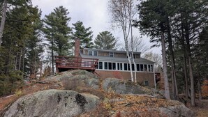 Eine Holzhütte mit einer Holzterrasse, umgeben von großen Steinen und Bäumen.