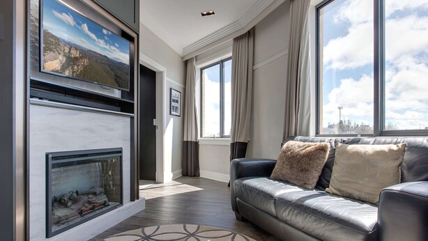 A modern living room with a fireplace, a leather sofa, and large windows offering a city view. - Perfect Located 2-bed Blue Mountains Getaway (Katoomba)