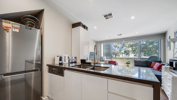 A modern kitchen with a stainless steel refrigerator, a built-in dishwasher, and a large window offering a view of the outdoors. - Tranquil Apartment in Green, Well Connected Suburb (Canberra)