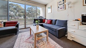 A modern living room with a grey sofa, a wooden coffee table, and a white TV stand. - Tranquil Apartment in Green, Well Connected Suburb (Canberra)