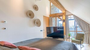 A bedroom with a large bed, a flat-screen TV, a chair, and a window with curtains. - Stylish Overnight Stay With a hot tub and Atmospheric Fireplace (De Koog)