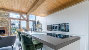 A modern kitchen with a large island, bar stools, and a stone fireplace. - Stylish Overnight Stay With a hot tub and Atmospheric Fireplace (De Koog)