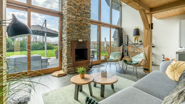 A spacious living area with a stone fireplace, large windows, and a cozy seating arrangement. - Stylish Overnight Stay With a hot tub and Atmospheric Fireplace (De Koog)