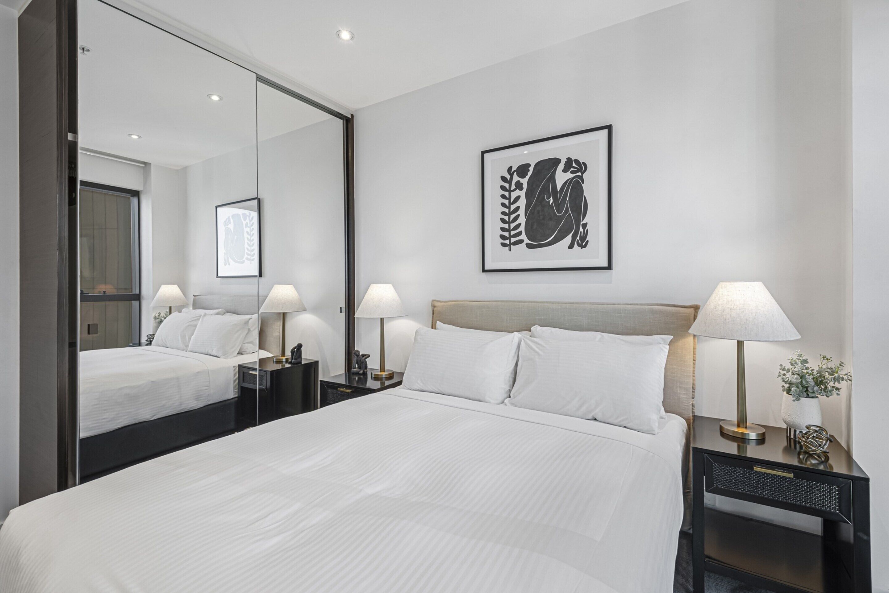 Habitación de hotel con una cama grande, dos mesitas de noche con lámparas, un espejo y una obra de arte enmarcada en la pared.