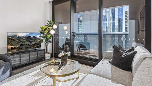 A modern living room with a large flat-screen TV, a glass coffee table, and a sofa.
