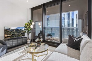 En moderne stue med et stort fladskærms-tv, et sofabord i glas og en sofa.