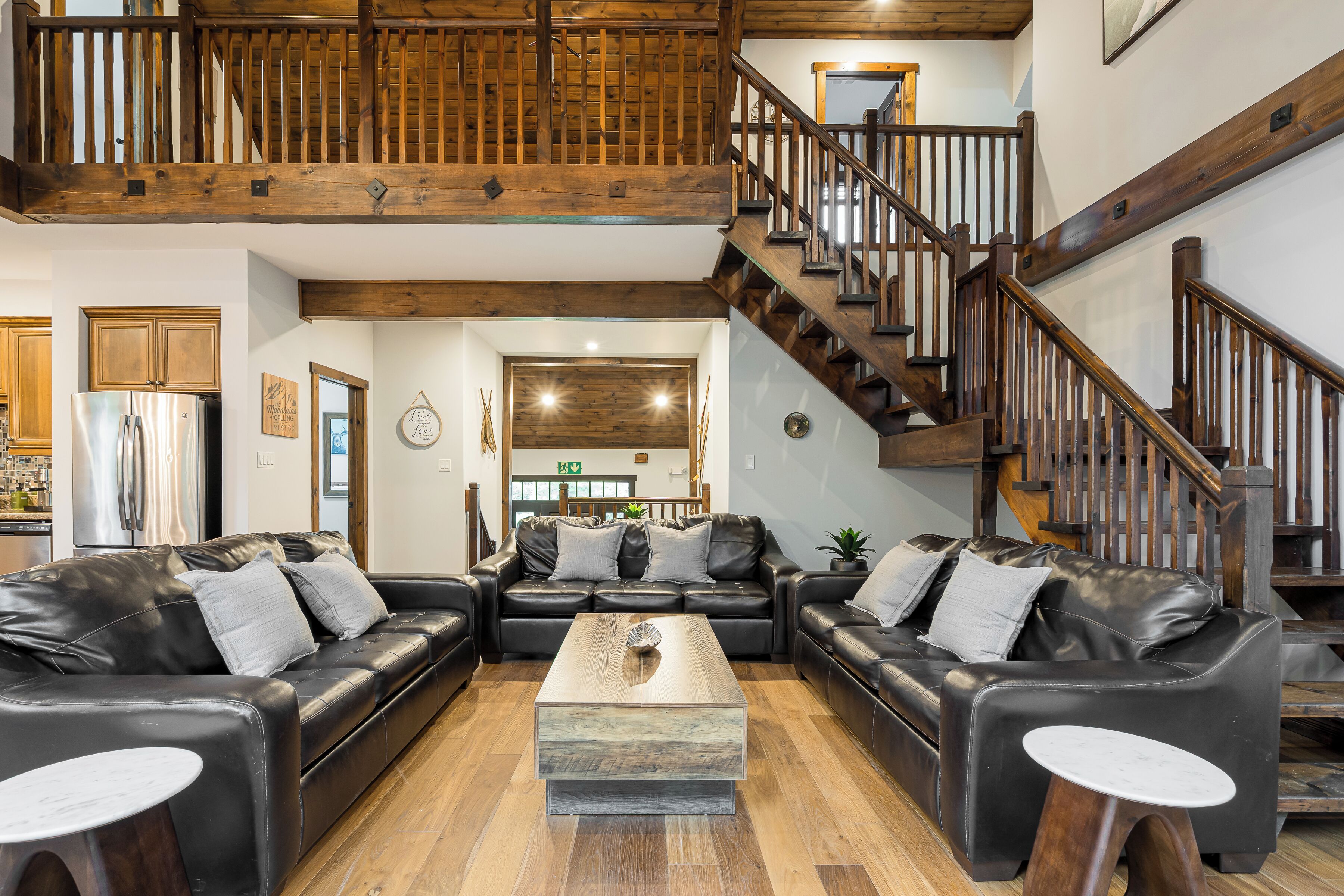 A spacious living area with leather sofas, a wooden coffee table, and a wooden staircase.