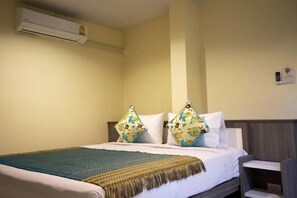A hotel room with a bed, two pillows with floral patterns, a woven throw blanket, a bedside table, and an air conditioning unit on the wall. - Samsen Sam Place (Bangkok)