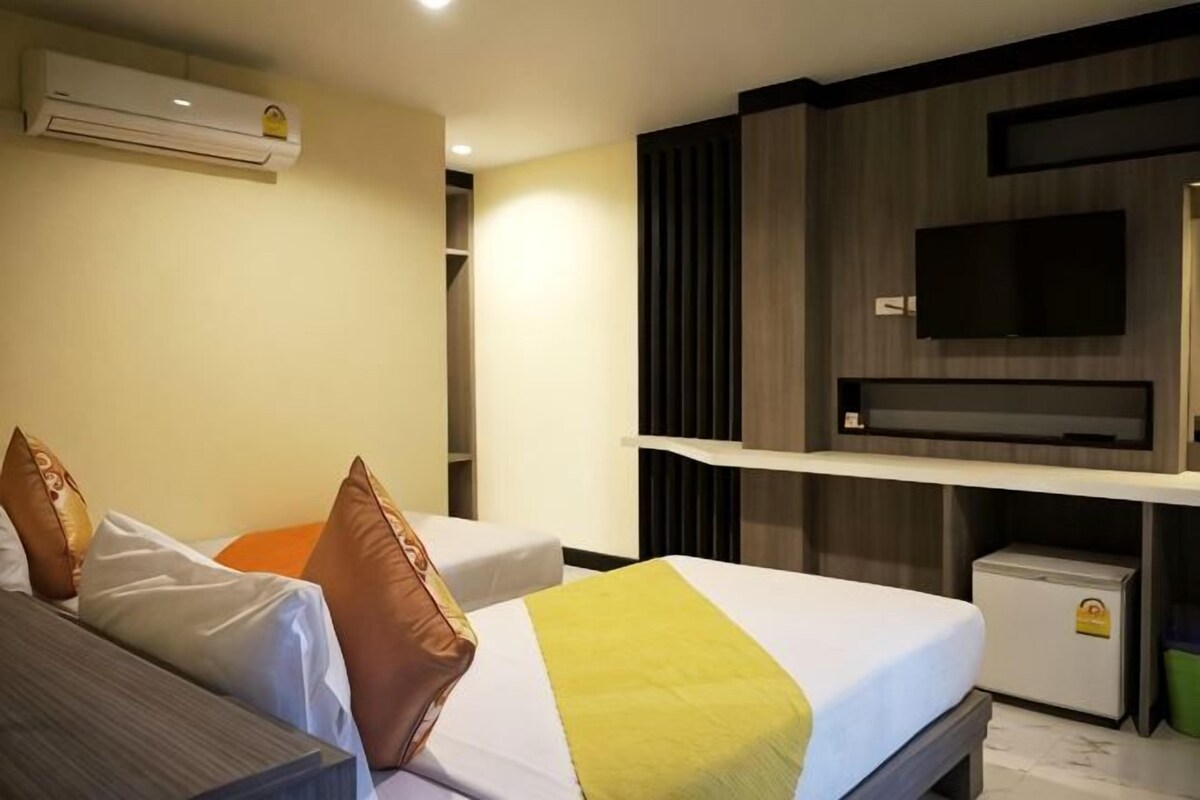 A hotel room with a bed, a desk, a TV, and an air conditioning unit.