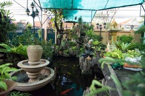 A greenhouse with a water feature, plants, and a decorative stone structure. - Samsen Sam Place (Bangkok)