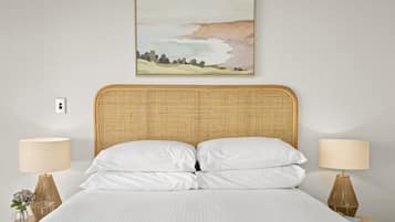 A neatly made bed with white linens, a woven headboard, and two bedside lamps on wooden nightstands.