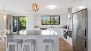 A modern kitchen with a central island, stainless steel appliances, and a view through a window. - Spacious 3-bed Home With Large Balcony (Hervey Bay)