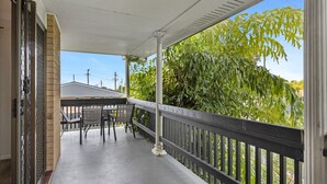 A covered outdoor area with a table and chairs, a railing, and a view of greenery and a building in the background. - Spacious 3-bed Home With Large Balcony (Hervey Bay)