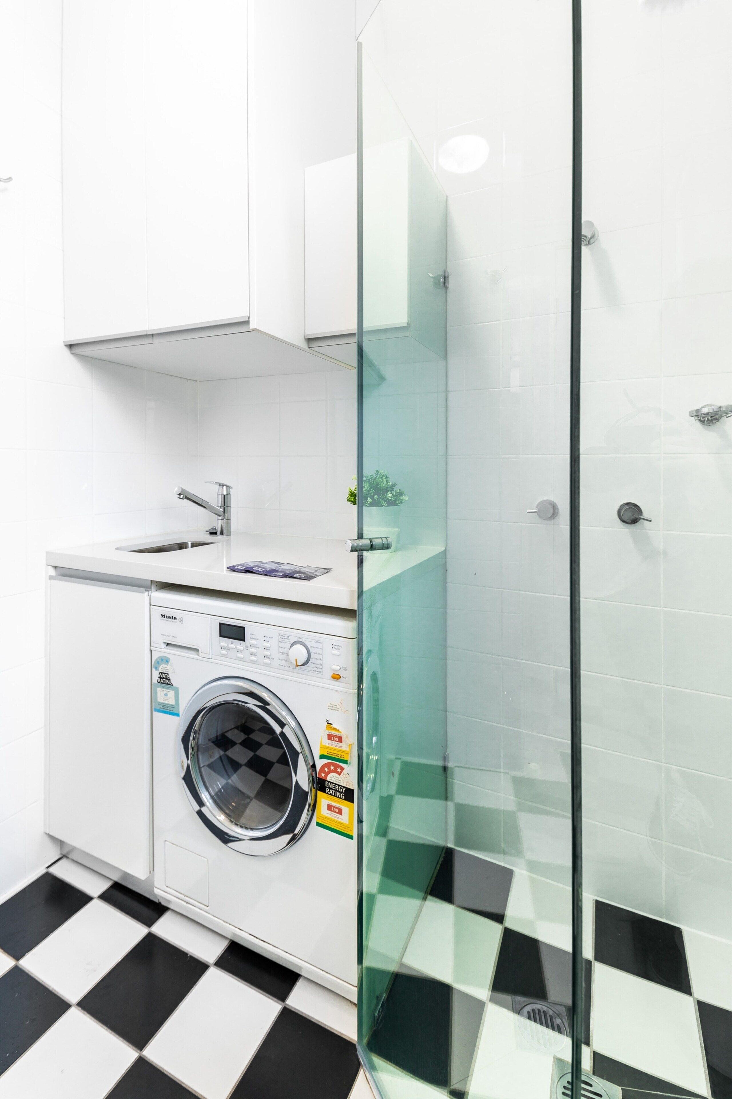 A modern bathroom with a glass shower enclosure, a washing machine, and a sink.