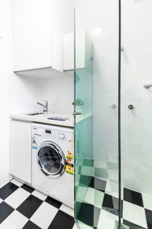 Une salle de bain moderne avec une douche à parois de verre, un lave-linge et un lavabo.