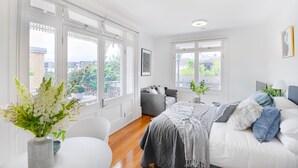 A bright, spacious bedroom with large windows, a bed, a sofa, and a dining table. - Perfect Located Studio Apartment (Sydney)