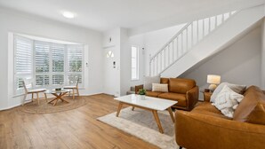 Ein geräumiges Wohnzimmer mit Holzboden, einem braunen Ledersofa, einem weißen Couchtisch und einem Essbereich mit rundem Tisch und Stühlen.