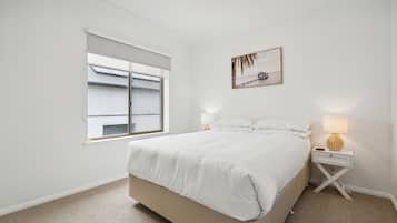 Un dormitorio con una cama, una mesita de noche, una lámpara, una ventana con persianas y un cuadro colgado en la pared.