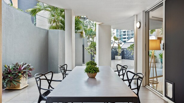 A modern dining area with a long table, black chairs, and a potted plant. - Comfy 2-bed With Pool and Secure Parking (Brisbane)