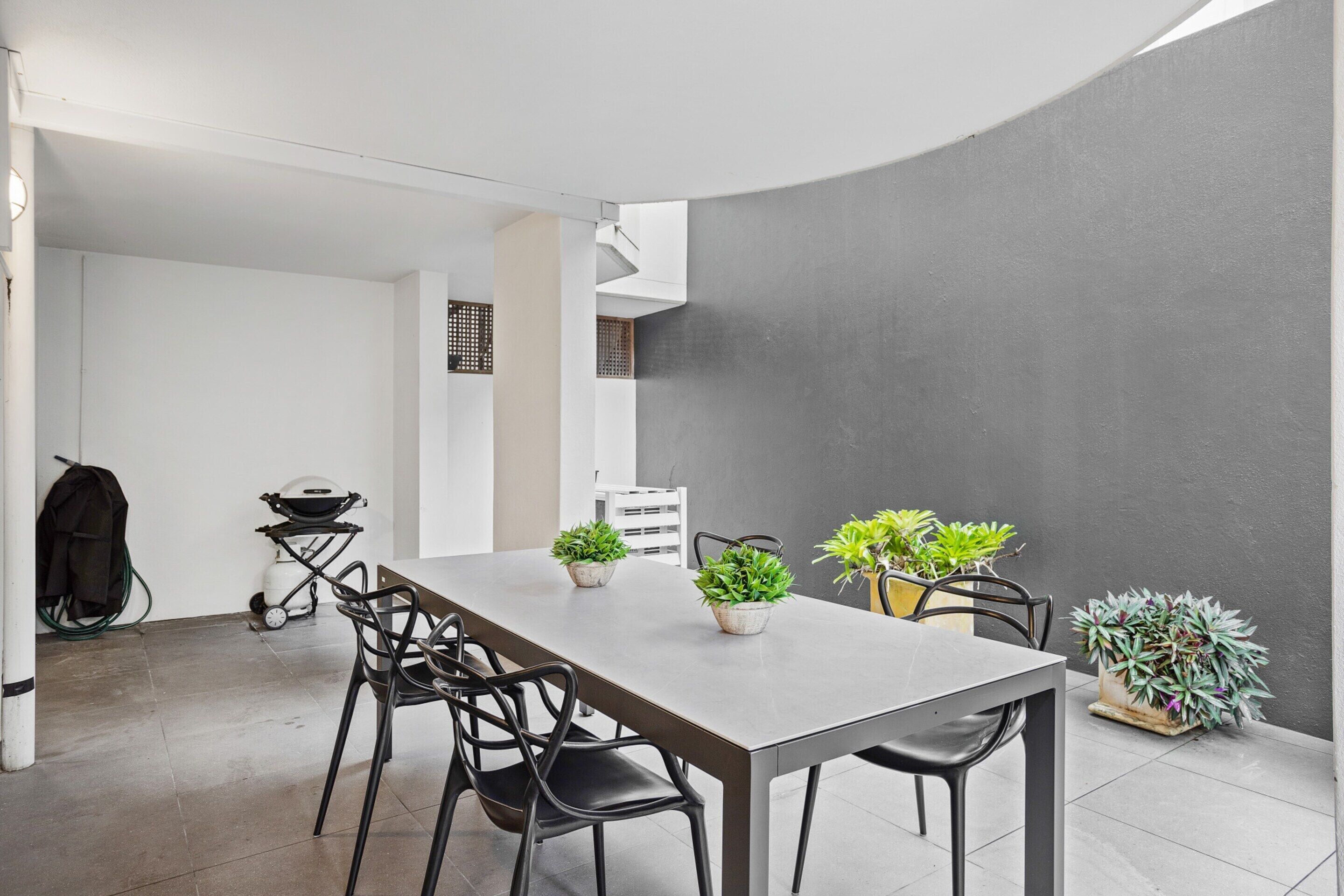 A modern dining area with a rectangular table, black chairs, and potted plants.