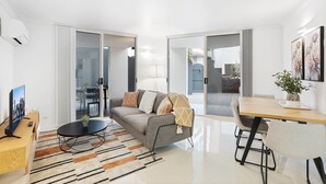 A modern living room with a sofa, coffee table, and a dining area with a table and chairs. - Comfy 2-bed With Pool and Secure Parking (Brisbane)