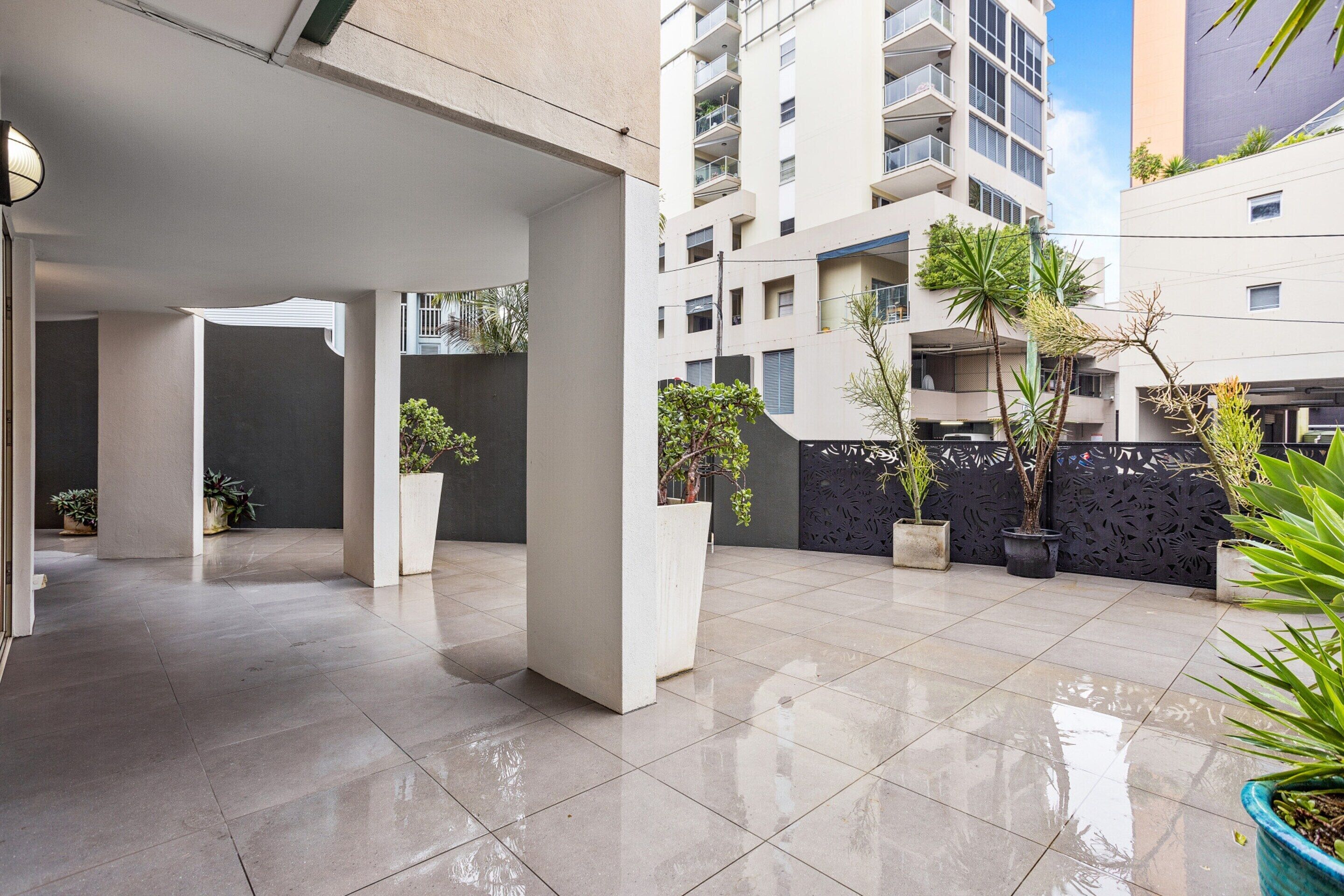 A modern urban courtyard with tiled flooring, concrete pillars, and potted plants.