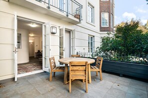 A wooden table and chairs set on a patio with a view of a building and a garden. - Modern East Melbourne 2-bed Apartment With Parking (Melbourne)